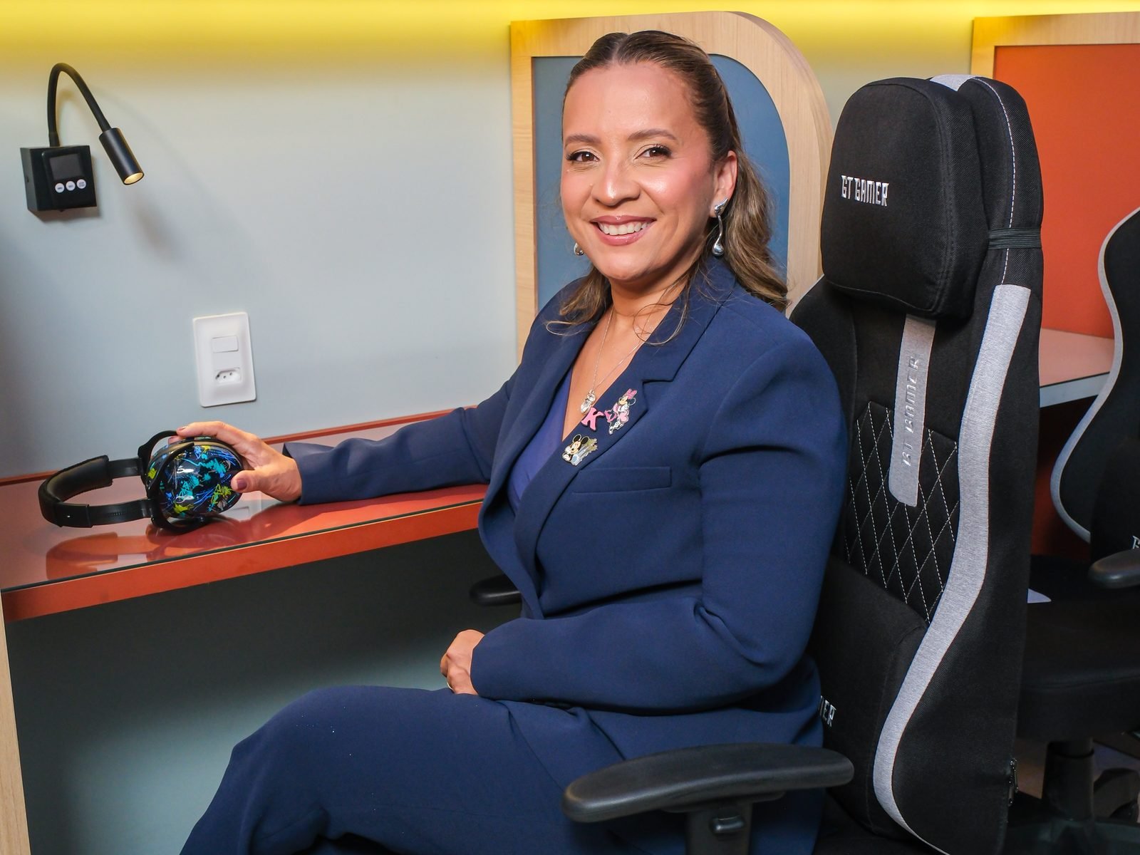 Kennya Martins sentada em uma cabine de estudo, com um fone de ouvido sobre a mesa