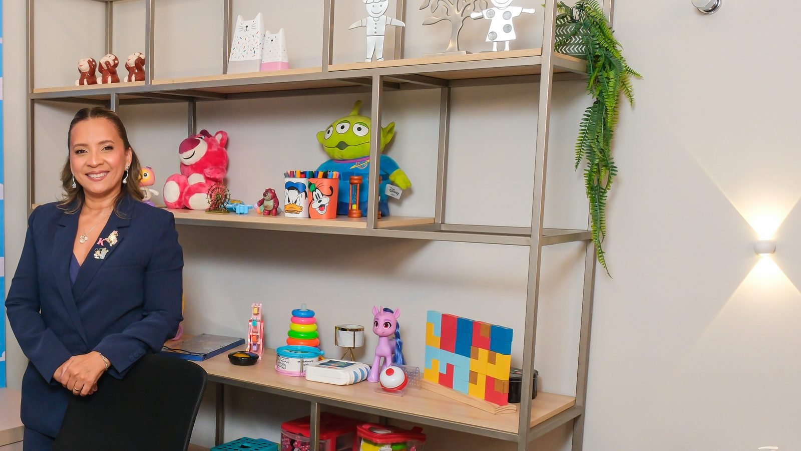 Kennya Martins em pé atrás da cadeira, ao lado da estante de jogos da sala infantil