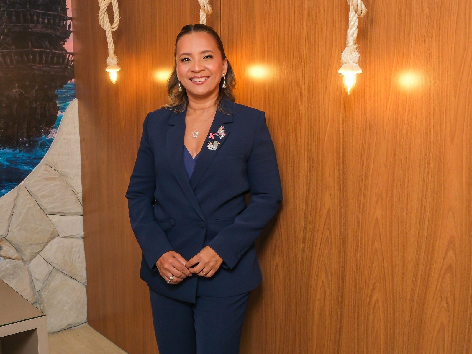 Kennya Martins, neuropsicóloga, sorrindo diante de um painel de madeira com luminárias de corda