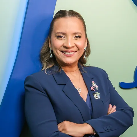 Kennya Martins sorrindo, em retrato com fundo verde e uma faixa azul